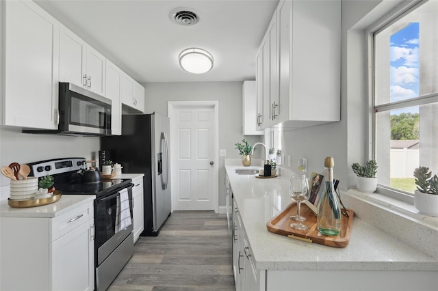 kitchen with visible vents, a sink, wood finished floors, white cabinetry, and appliances with stainless steel finishes