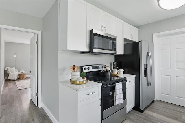 kitchen with light wood-style flooring, stainless steel appliances, white cabinets, light countertops, and baseboards