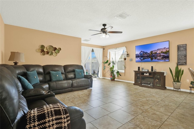 living room featuring a textured ceiling, light tile patterned floors, visible vents, baseboards, and a ceiling fan