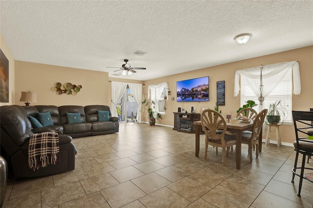 tiled living room with a ceiling fan, visible vents, a textured ceiling, and baseboards