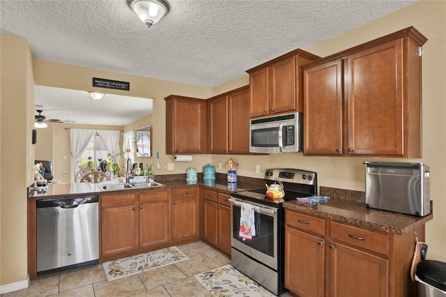 kitchen with dark stone counters, stainless steel appliances, brown cabinetry, and a sink