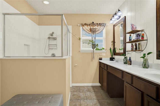 bathroom with a textured ceiling, double vanity, tiled shower, and a sink