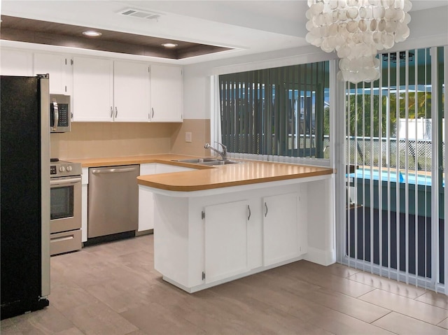 kitchen featuring a sink, white cabinets, light countertops, appliances with stainless steel finishes, and a tray ceiling