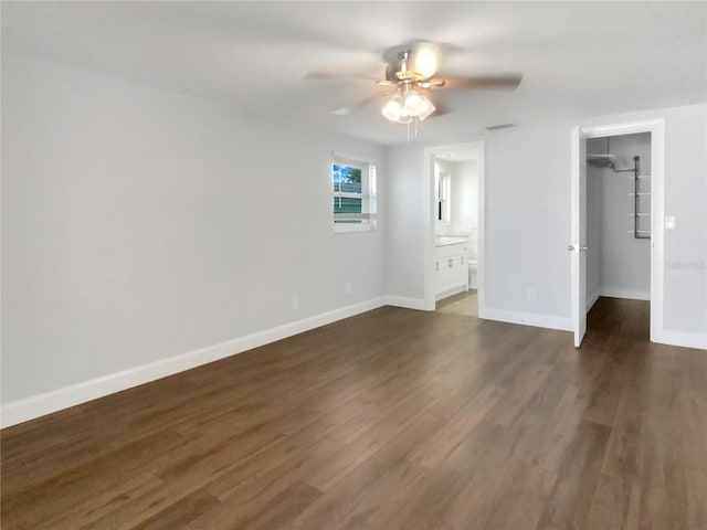 unfurnished bedroom with baseboards, a ceiling fan, dark wood-style floors, ensuite bath, and a walk in closet