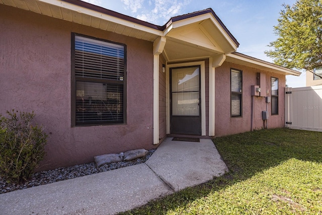 view of exterior entry with fence, a lawn, and stucco siding