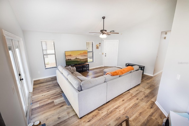 living room featuring light wood-style floors, vaulted ceiling, baseboards, and ceiling fan