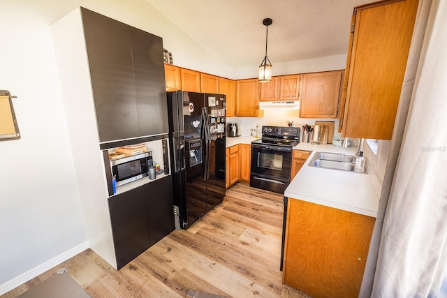 kitchen with light countertops, a sink, light wood-type flooring, under cabinet range hood, and black appliances