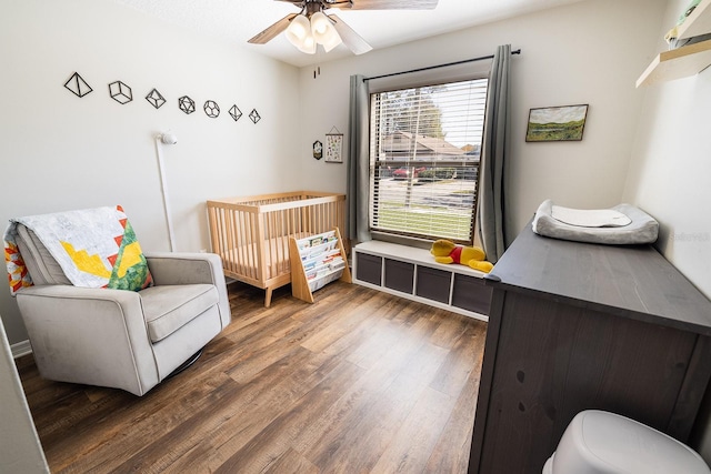 bedroom with a crib, wood finished floors, and a ceiling fan