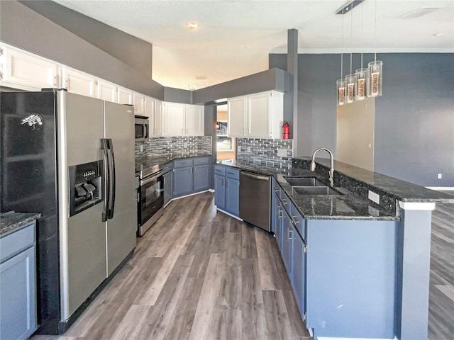 kitchen featuring white cabinets, appliances with stainless steel finishes, dark stone countertops, a peninsula, and a sink