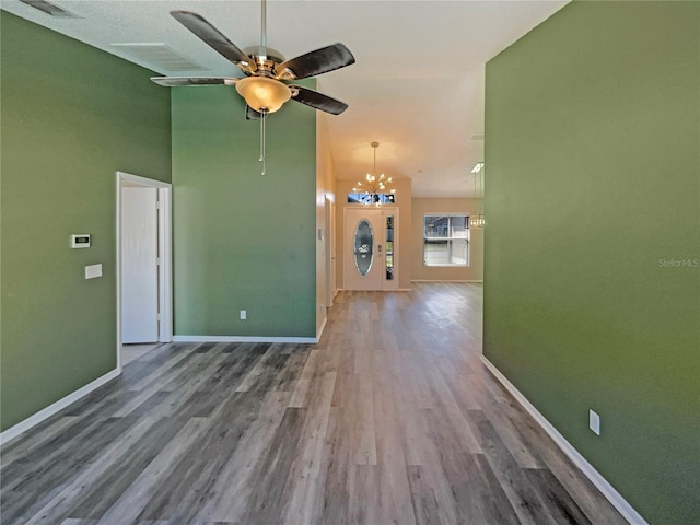 empty room with ceiling fan with notable chandelier, visible vents, baseboards, and wood finished floors