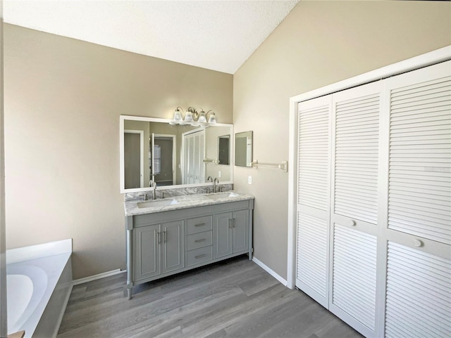 full bath with double vanity, a bath, a sink, and wood finished floors