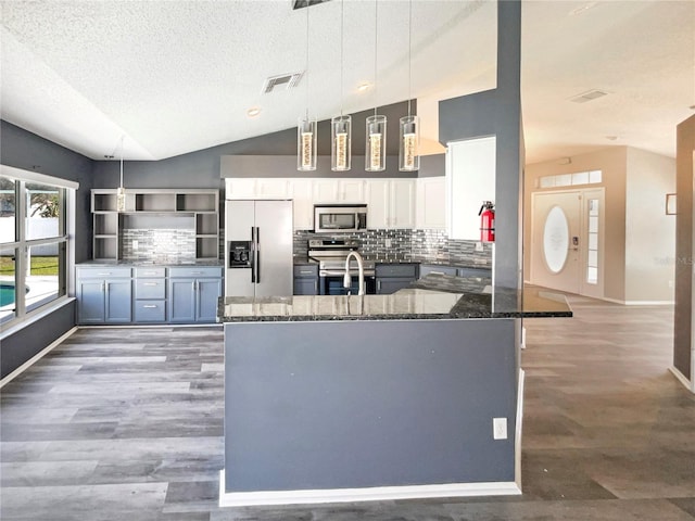 kitchen featuring vaulted ceiling, stainless steel appliances, tasteful backsplash, and dark stone countertops