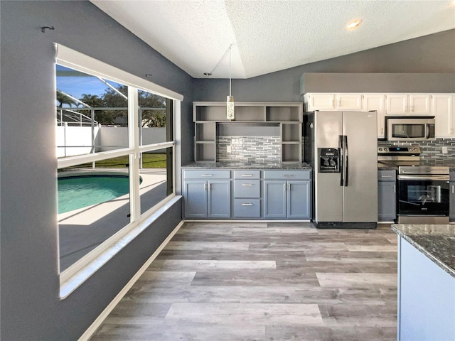 kitchen with white cabinetry, light wood-style floors, vaulted ceiling, appliances with stainless steel finishes, and tasteful backsplash