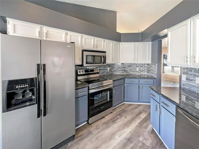 kitchen with stainless steel appliances, dark stone countertops, backsplash, and white cabinetry