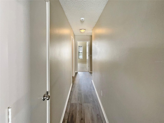 corridor with dark wood-style flooring, a textured ceiling, and baseboards