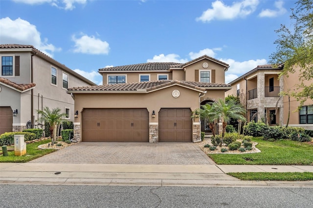 mediterranean / spanish-style home with stone siding, an attached garage, and decorative driveway