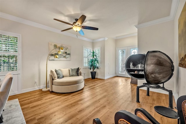 living area featuring a ceiling fan, baseboards, light wood-type flooring, and ornamental molding