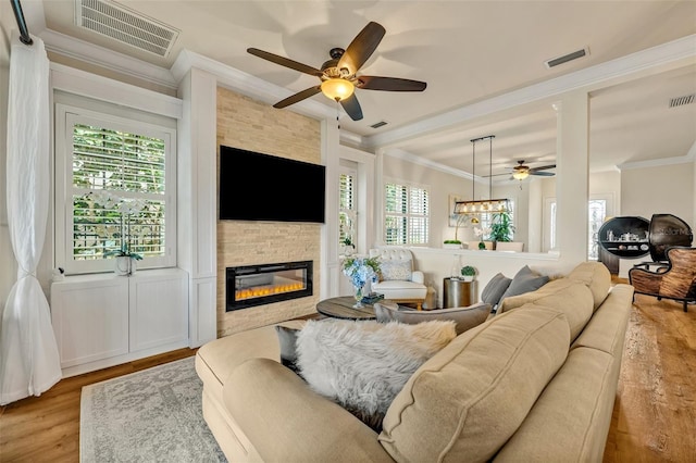 living room featuring visible vents, a stone fireplace, wood finished floors, and crown molding