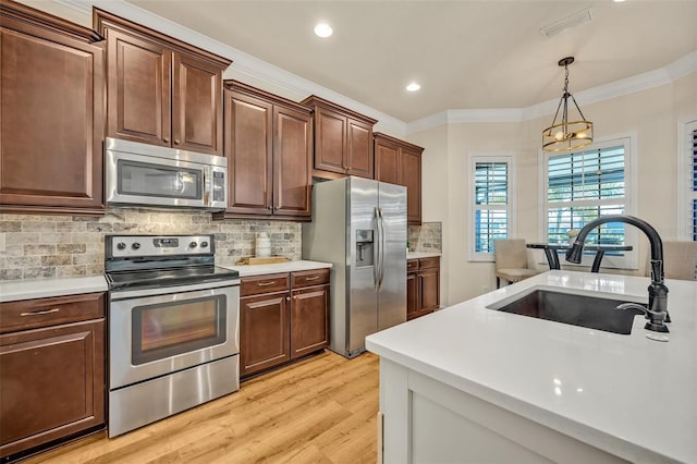 kitchen with ornamental molding, stainless steel appliances, light countertops, and a sink