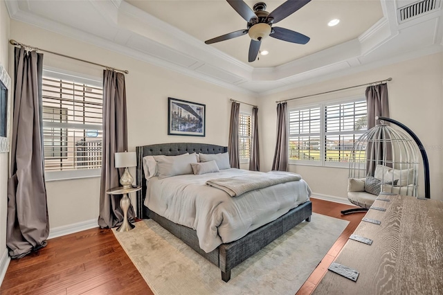 bedroom with a tray ceiling, crown molding, wood finished floors, and visible vents