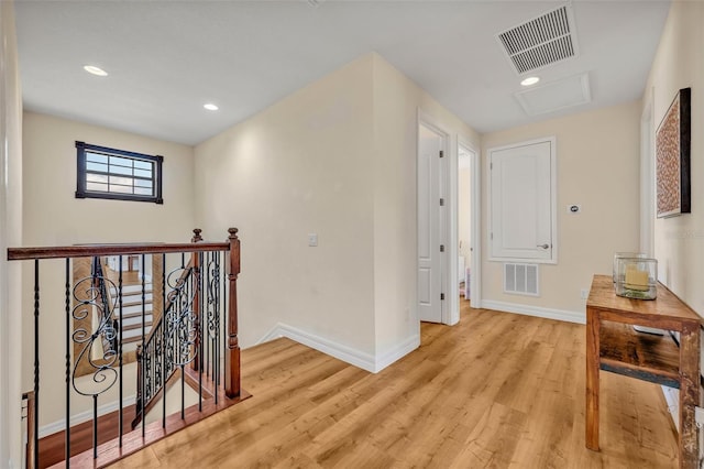 hall with light wood-type flooring, visible vents, an upstairs landing, and baseboards