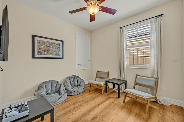 sitting room with baseboards, light wood-type flooring, and ceiling fan