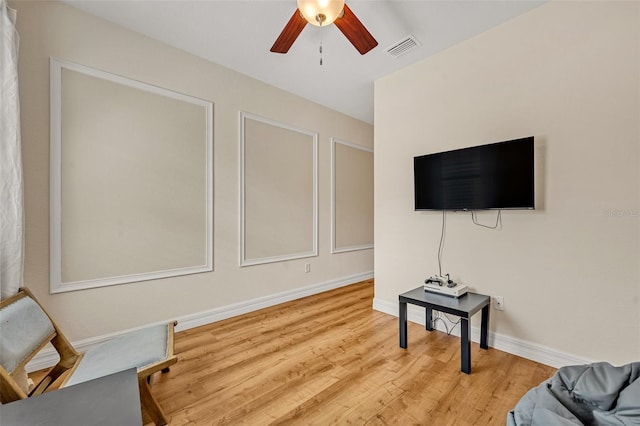 living area featuring visible vents, baseboards, a ceiling fan, and wood finished floors