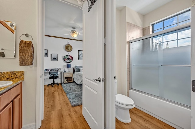 bathroom featuring toilet, a ceiling fan, wood finished floors, enclosed tub / shower combo, and vanity