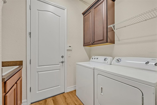 clothes washing area with baseboards, light wood-style flooring, separate washer and dryer, cabinet space, and a sink