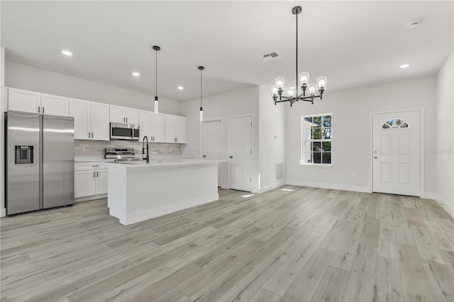 kitchen featuring tasteful backsplash, light countertops, light wood-style flooring, appliances with stainless steel finishes, and white cabinetry