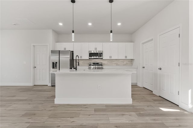 kitchen with white cabinets, stainless steel appliances, light countertops, and an island with sink