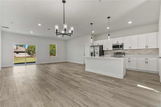 kitchen featuring stainless steel appliances, white cabinetry, open floor plan, decorative backsplash, and light wood finished floors