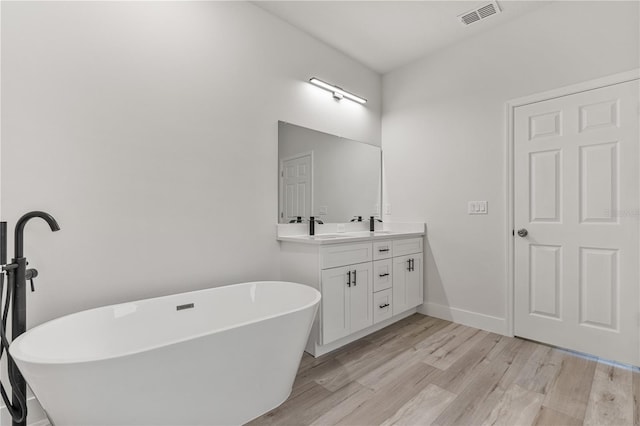 bathroom featuring baseboards, visible vents, wood finished floors, vanity, and a freestanding tub