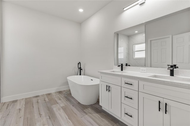 full bath featuring double vanity, wood finished floors, a soaking tub, and a sink