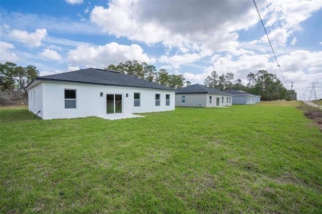 back of property with a shingled roof and a lawn