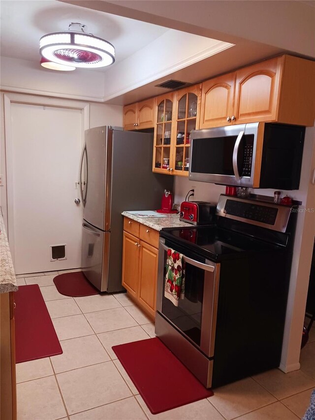 kitchen featuring light tile patterned floors, visible vents, glass insert cabinets, stainless steel appliances, and light countertops