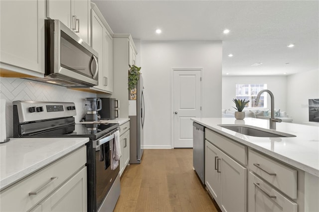 kitchen with light wood-type flooring, a sink, stainless steel appliances, decorative backsplash, and light stone countertops