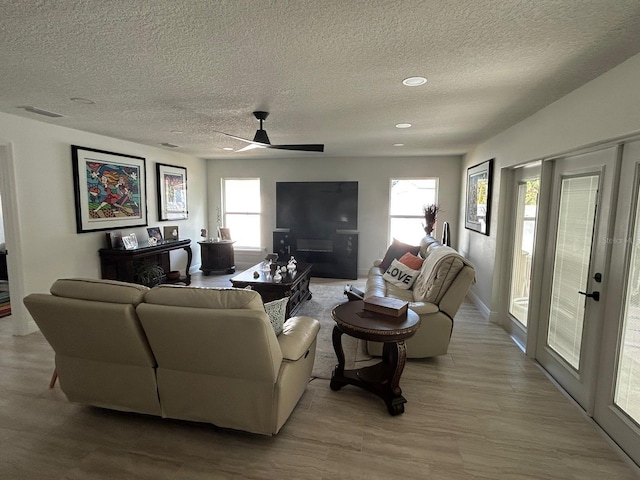 living room featuring plenty of natural light, visible vents, light wood-style flooring, and a ceiling fan