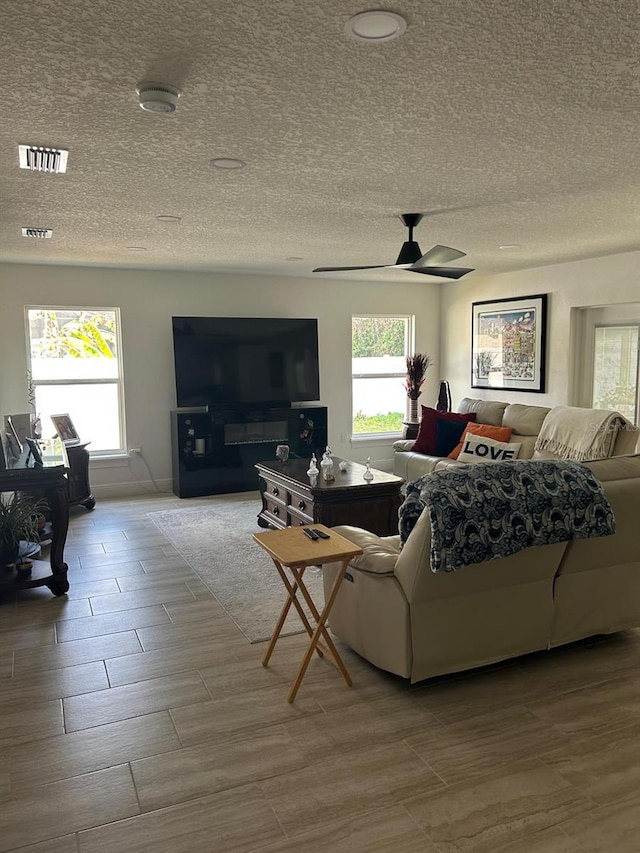 living room featuring a textured ceiling, ceiling fan, plenty of natural light, and visible vents