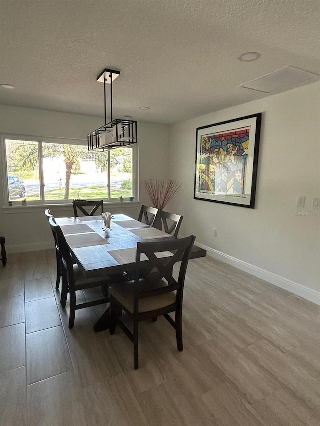 dining space featuring light wood-style floors, baseboards, and a textured ceiling