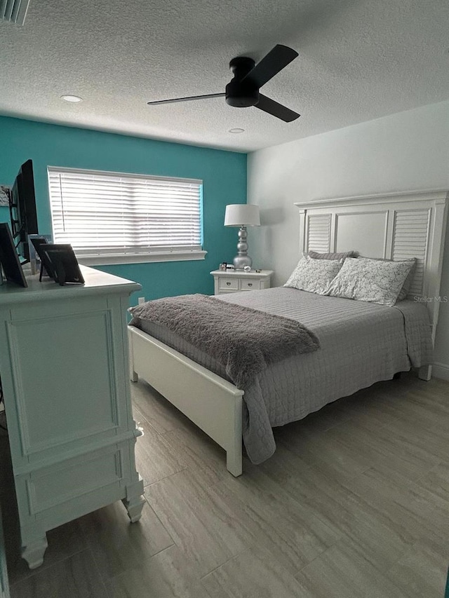 bedroom with light wood-style floors, visible vents, ceiling fan, and a textured ceiling