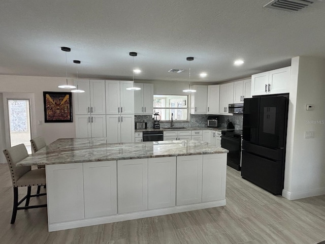 kitchen featuring a sink, visible vents, white cabinets, black appliances, and tasteful backsplash