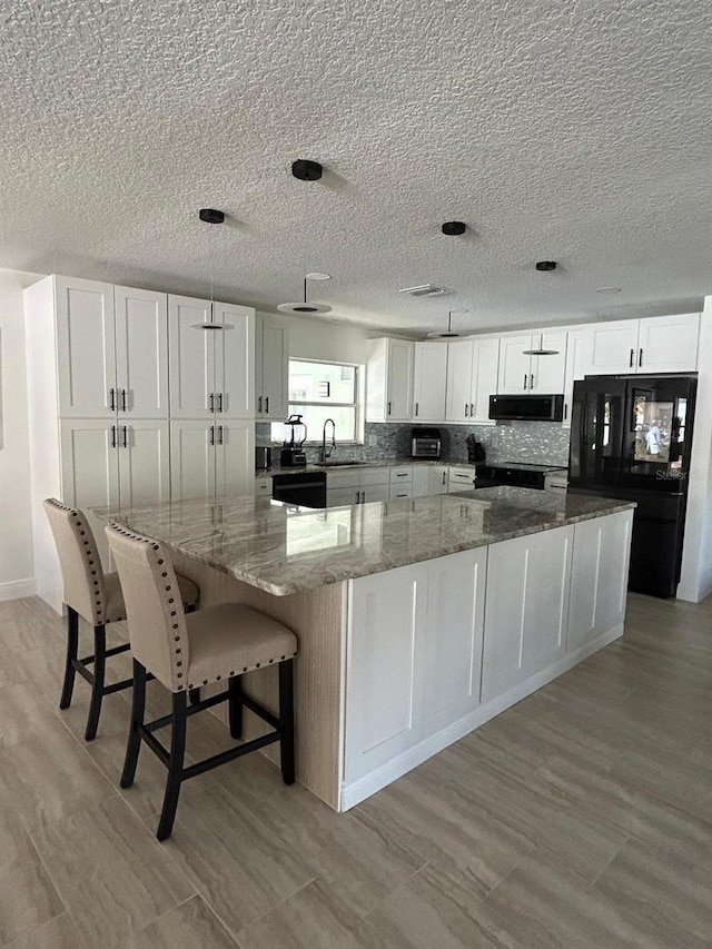 kitchen featuring a spacious island, backsplash, white cabinetry, a sink, and black appliances