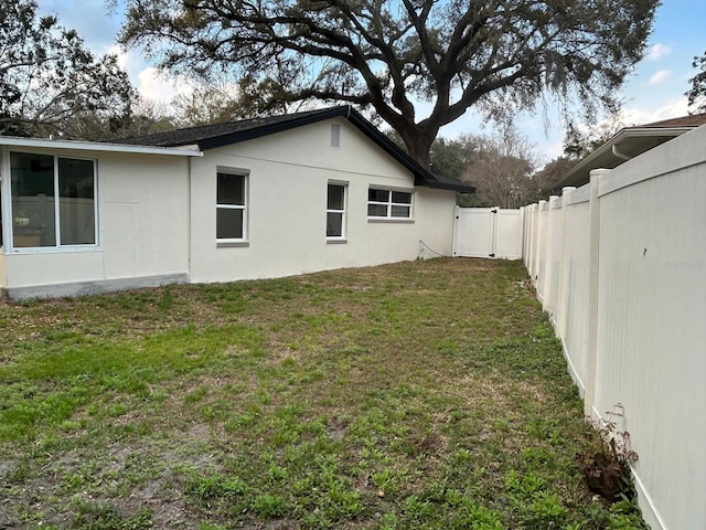 view of side of property featuring a yard, a fenced backyard, and stucco siding