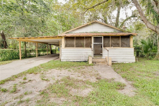 view of front of home with a sunroom, a view of trees, a carport, and concrete driveway