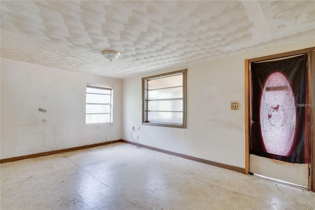 spare room with a textured ceiling, tile patterned floors, and baseboards