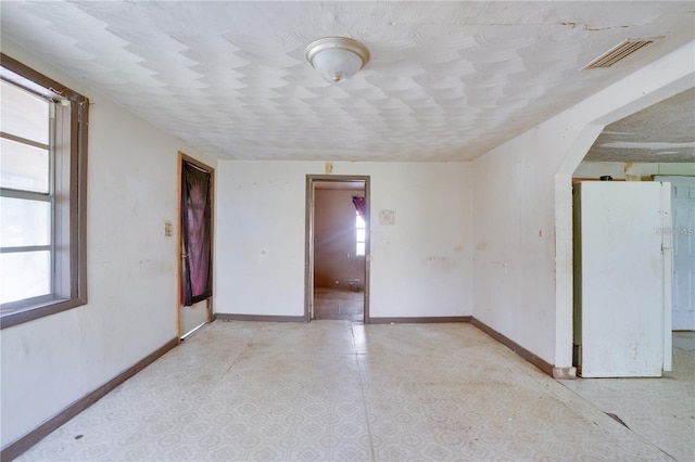 unfurnished room featuring a wealth of natural light, visible vents, arched walkways, and baseboards