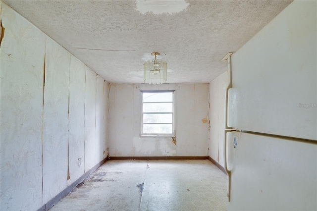 unfurnished room with baseboards, a chandelier, and a textured ceiling