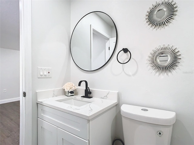 half bath featuring toilet, wood finished floors, and vanity