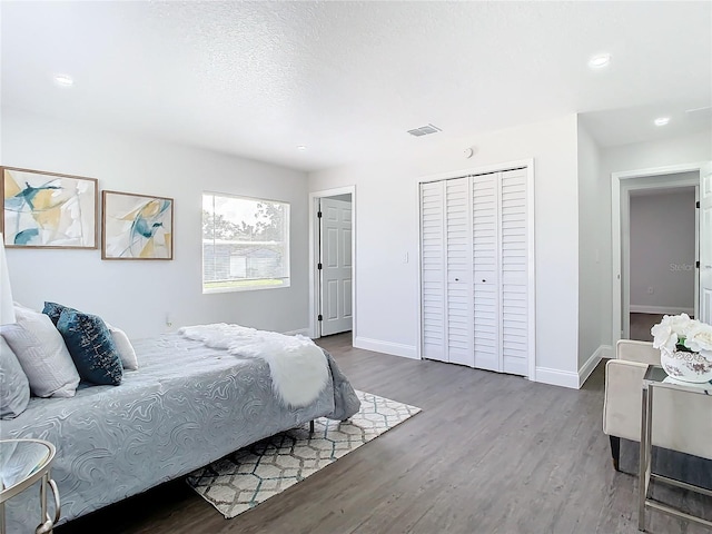 bedroom with a closet, visible vents, a textured ceiling, wood finished floors, and baseboards